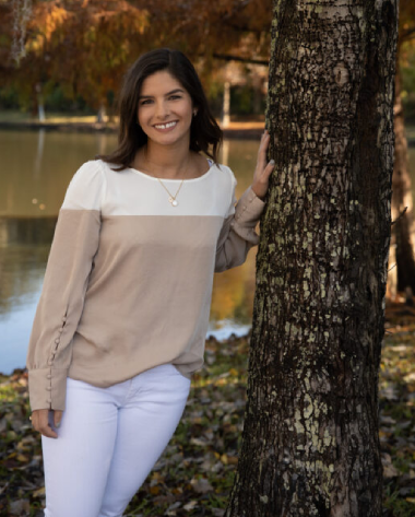 A woman leaning against a tree in front of the water.