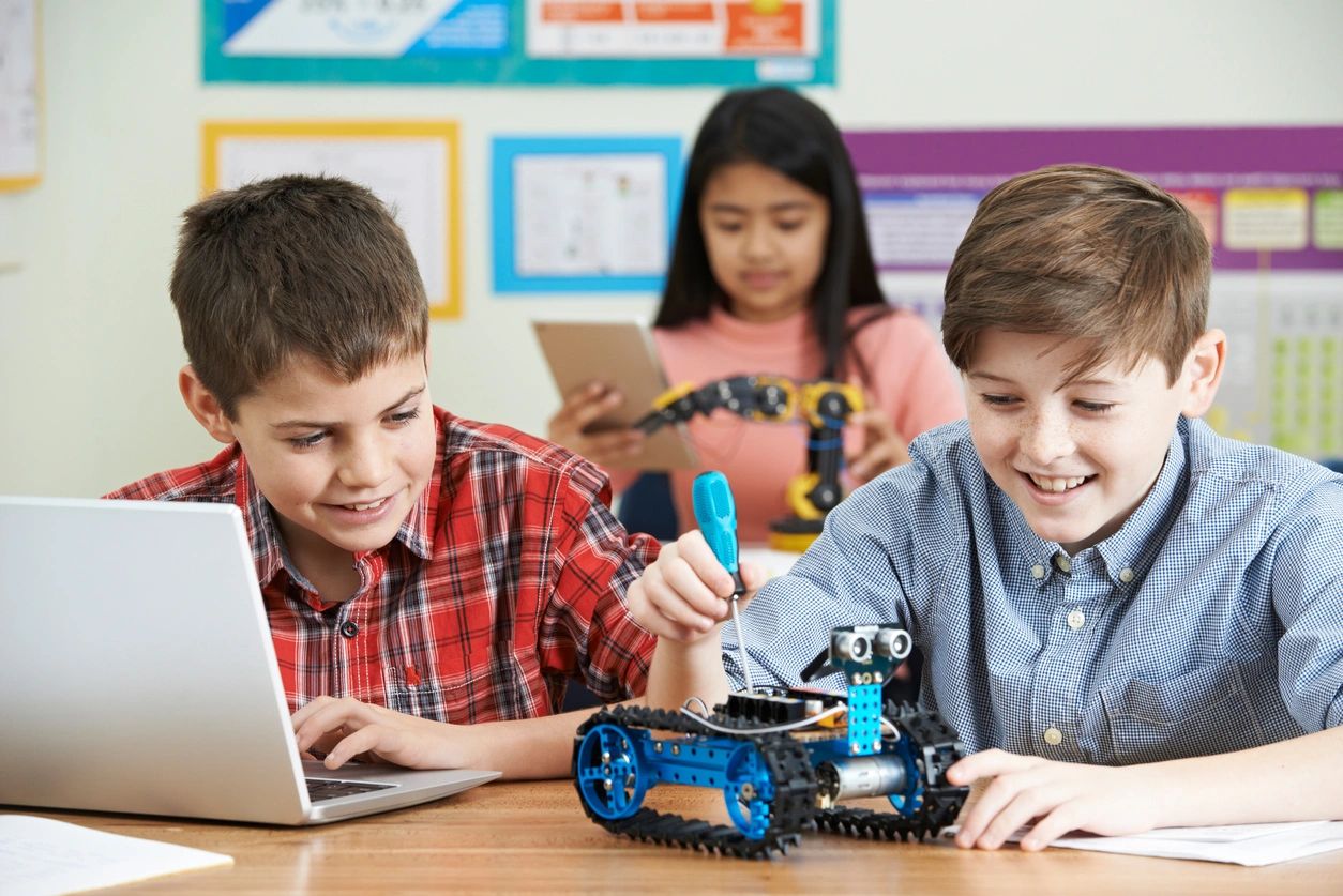 A group of kids sitting at a table with laptops.